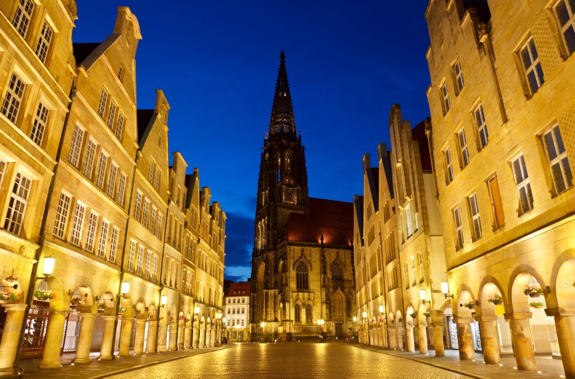 Die Lambertikirche in Münster in der Dämmerung zwischen beleuchteten Straßen.