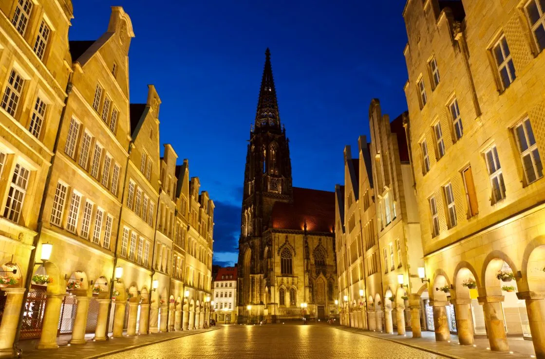 Die Lambertikirche in Münster in der Dämmerung zwischen beleuchteten Straßen.