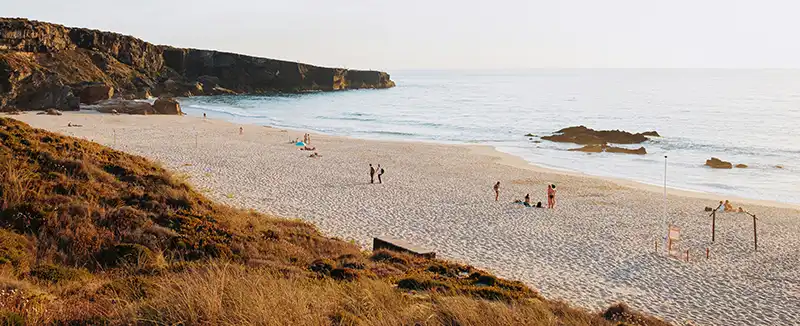 Gruppo di persone che si rilassa su una spiaggia portoghese sotto il sole, godendo la brezza marina