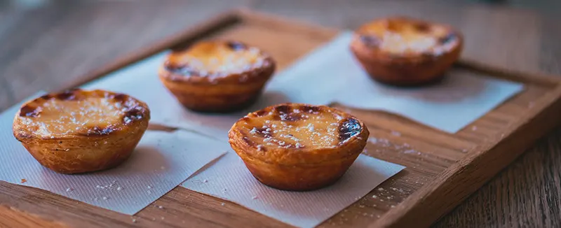 Quattro pastéis de nata disposti su un vassoio di legno