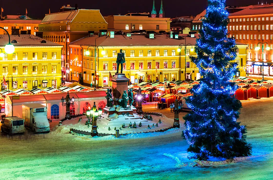 Helsingin Senaatintori talvi-iltana, joulukuusi ja Joulutorin valaistut myyntikojut historiallisten rakennusten ympäröimänä.
