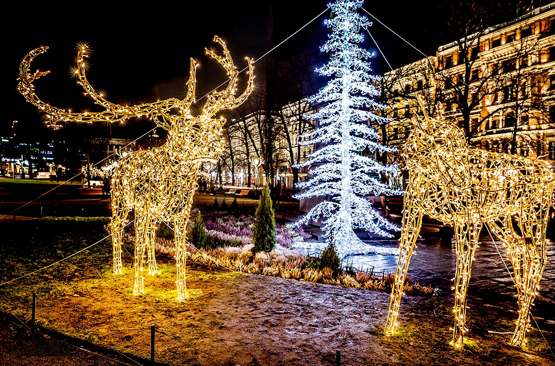 Helsingin keskustan jouluvalot, valaistut hirvifiguurit ja loistava valokuusi pimeässä talvi-illassa.