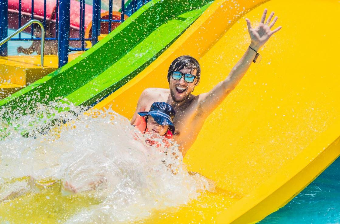 Mann rutscht mit Sohn im Wasserpark.