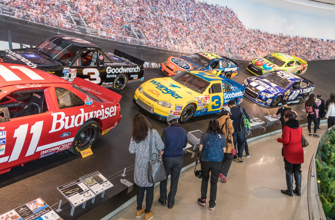 An installation showing a section of banked racing circuit, with a number of racing cars on it